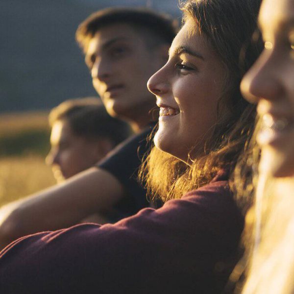 Jóvenes sonriendo en un campo al atardecer, disfrutando del aire libre y la amistad.